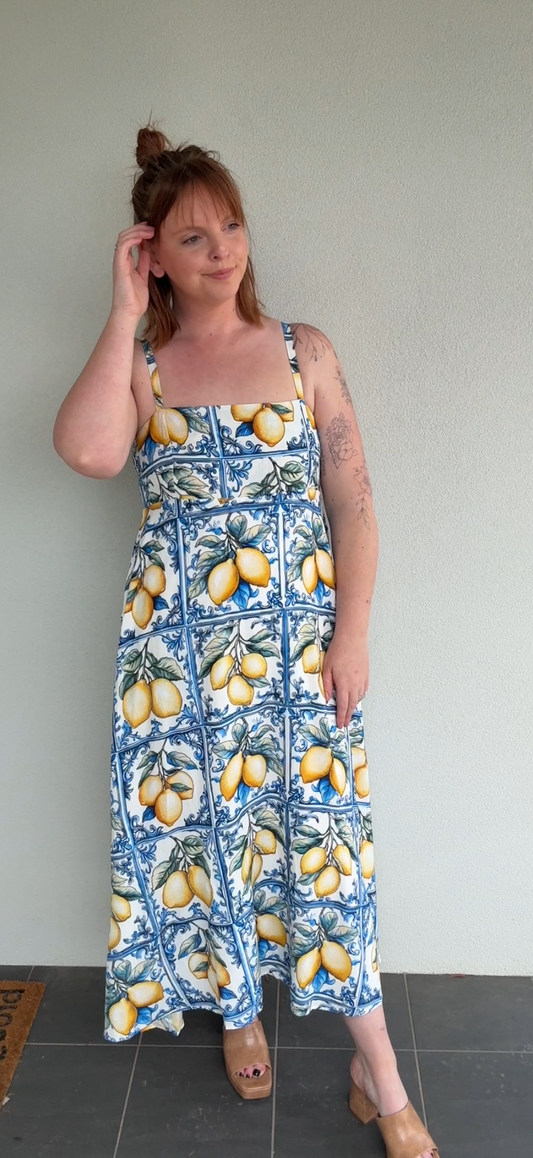 Woman wearing a floral dress with lemons in front of a plain wall.
